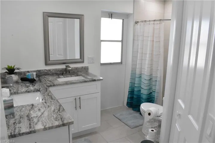 Full bath featuring double vanity, light tile patterned floors, and a shower with curtain