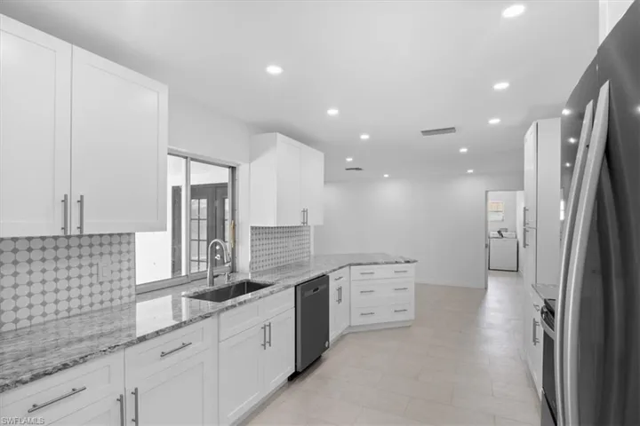 Kitchen featuring appliances with stainless steel finishes, tasteful backsplash, light stone counters, white cabinetry, and recessed lighting