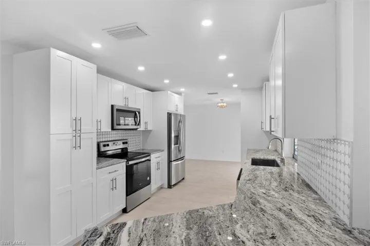 Kitchen featuring backsplash, light stone counters, appliances with stainless steel finishes, recessed lighting, and white cabinets