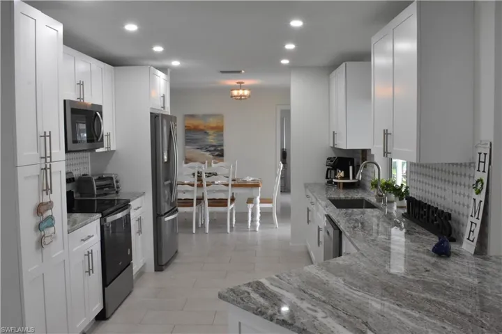 Kitchen featuring backsplash, stainless steel appliances, light stone countertops, recessed lighting, and white cabinets