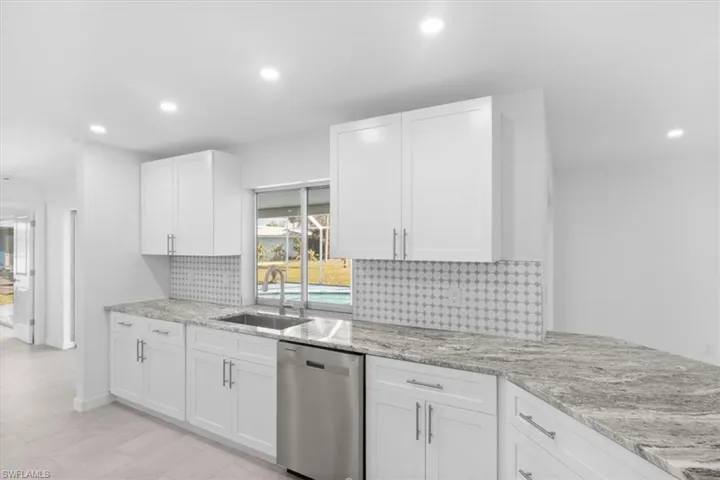 Kitchen with tasteful backsplash, dishwasher, white cabinets, light stone counters, and recessed lighting