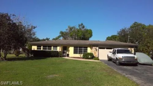 Ranch-style residence featuring a pale yellow exterior, a shingled roof, and an attached garage
