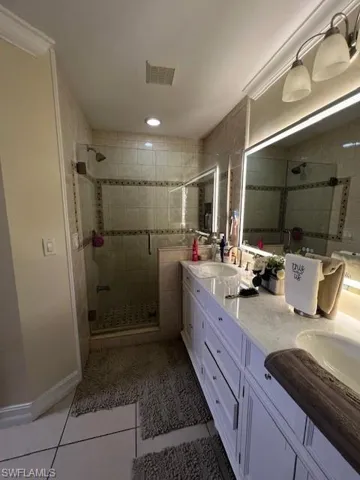 Full bath with double vanity, light tile patterned flooring, and a stall shower