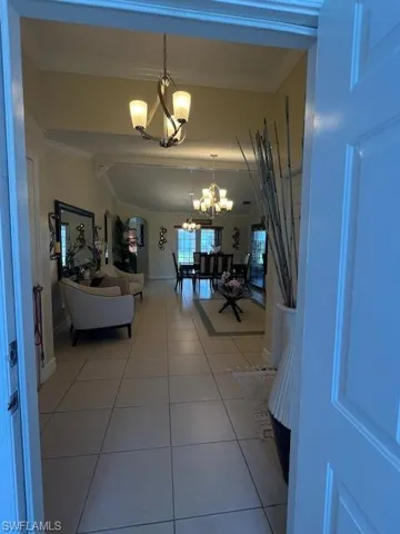 Hall with suspended lighting, light tile patterned floors, lofted ceiling, and crown molding