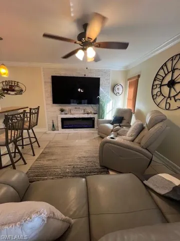Living area with light tile patterned floors, crown molding, a ceiling fan, and a fireplace