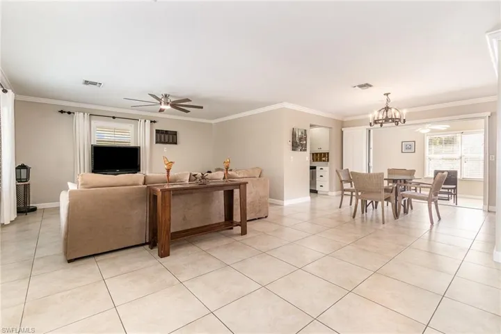 Living room featuring ceiling fan with notable chandelier, ornamental molding, and light tile patterned flooring