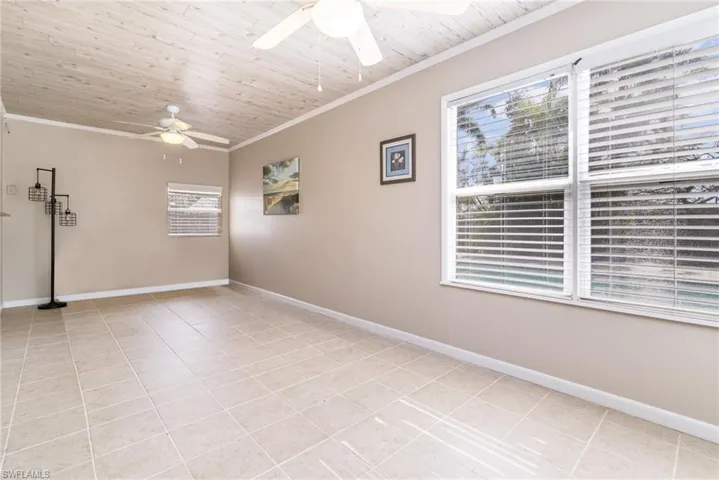 Empty room with light tile patterned floors, wood ceiling, ornamental molding, and ceiling fan