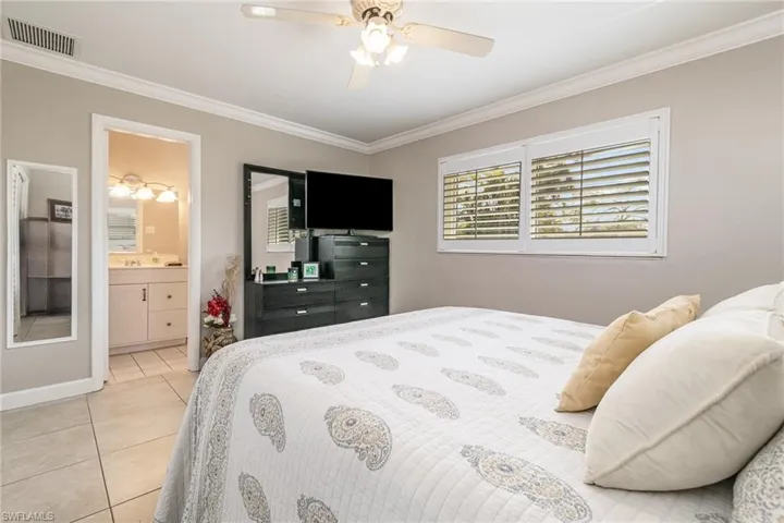 Tiled bedroom featuring ceiling fan, ornamental molding, and ensuite bathroom