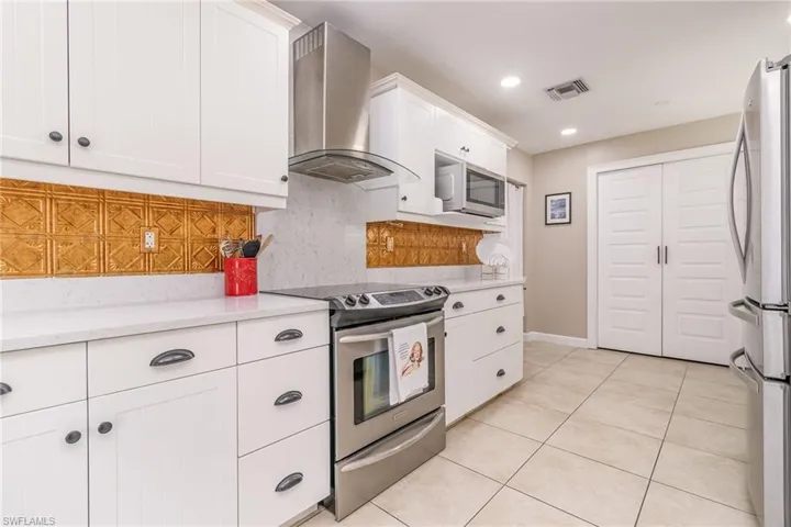 Kitchen featuring ventilation hood, tasteful backsplash, white cabinets, light tile patterned floors, and stainless steel appliances