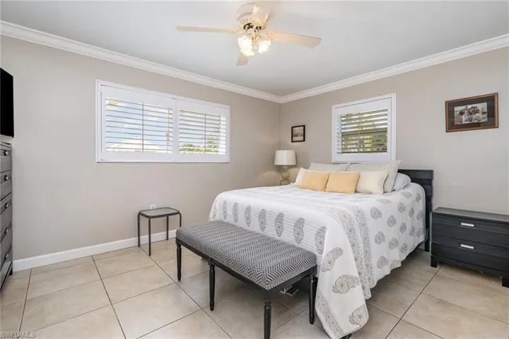 Tiled bedroom featuring ceiling fan and ornamental molding