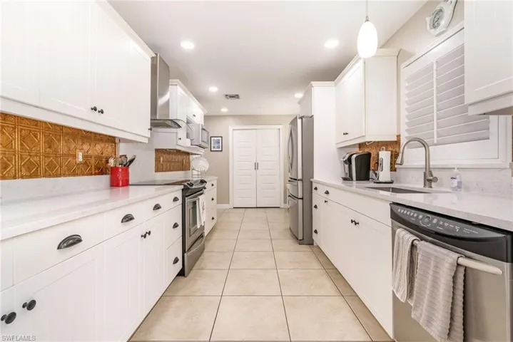 Kitchen featuring wall chimney range hood, sink, appliances with stainless steel finishes, hanging light fixtures, and white cabinets