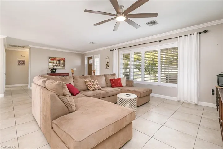 Living room with crown molding, light tile patterned floors, and ceiling fan
