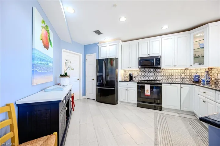 Kitchen featuring refrigerator with ice dispenser, black electric range, white cabinets, stainless steel microwave, and glass insert cabinets
