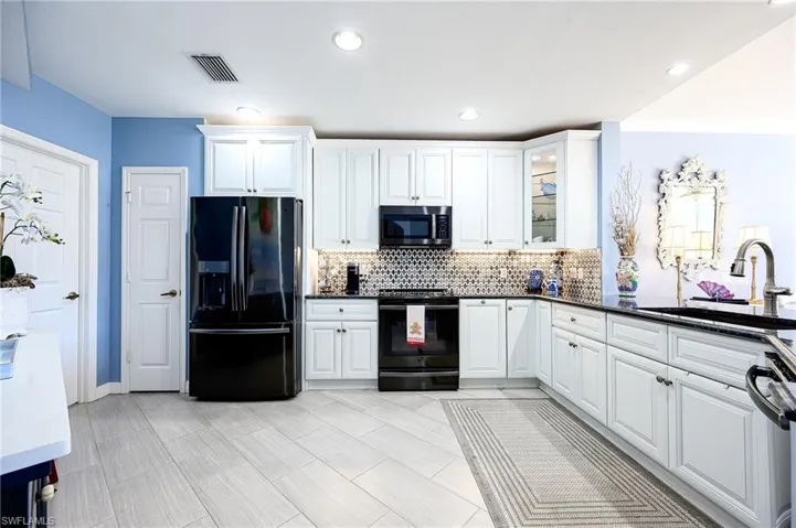 Kitchen with black appliances, white cabinets, glass insert cabinets, dark granite counters, and beautiful stone backsplash