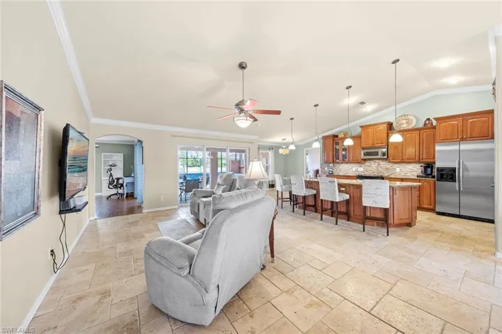 Living area featuring baseboards, a ceiling fan, crown molding, stone tile floors, and lofted ceiling