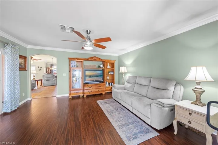 Living room with arched walkways, ornamental molding, ceiling fan, and wood finished floors