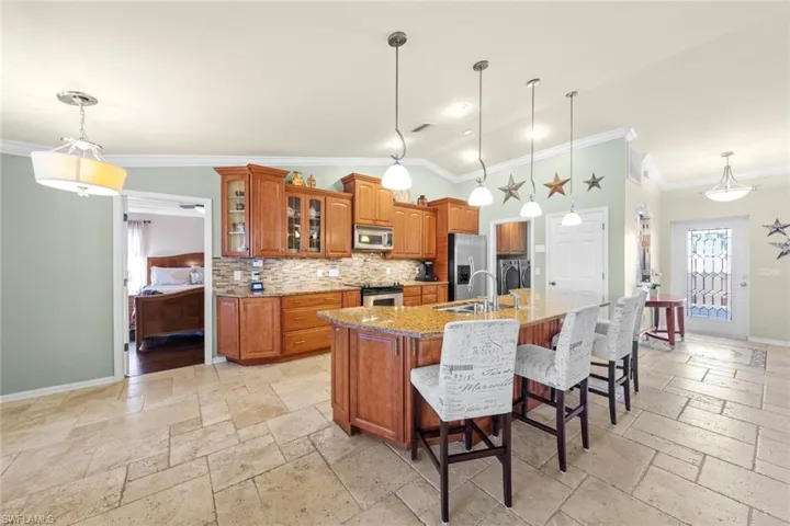 Kitchen featuring crown molding, stone tile floors, a sink, stainless steel appliances, and brown cabinets