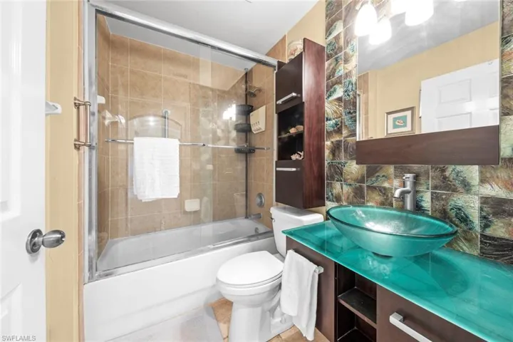 Bathroom with shower / bath combination with glass door, tasteful backsplash, tile walls, toilet, and vanity