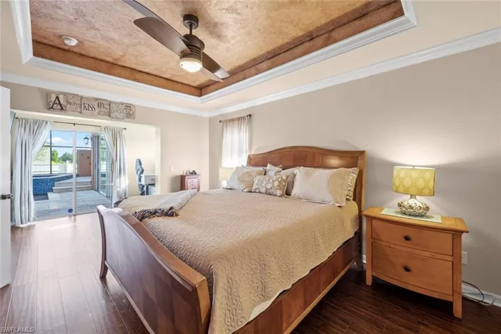 Bedroom featuring a raised ceiling, ceiling fan, crown molding, dark wood-type flooring, and access to outside