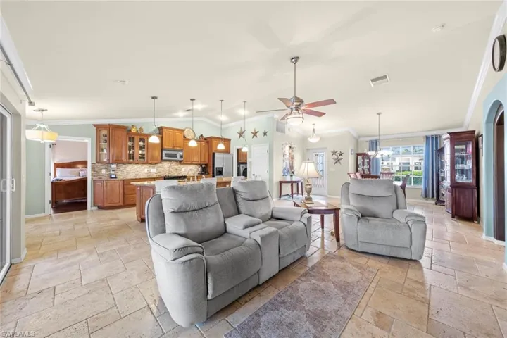Living room featuring crown molding, stone tile floors, ceiling fan with notable chandelier, and baseboards