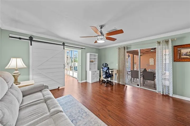 Living room featuring baseboards, ornamental molding, a ceiling fan, a barn door, and wood finished floors
