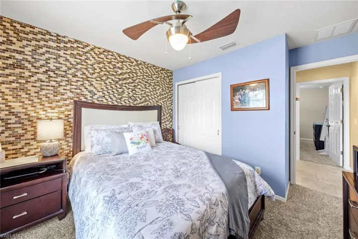 Carpeted bedroom featuring visible vents, an accent wall, a closet, baseboards, and ceiling fan