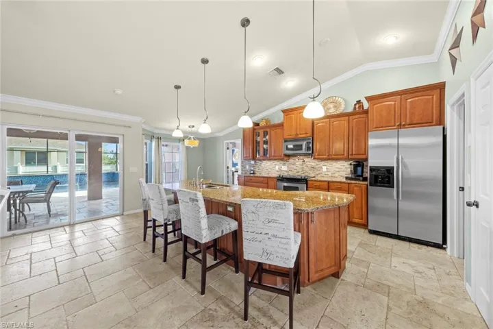 Kitchen featuring travertrine tile flooring, an island with sink, brown cabinets, and stainless steel appliances