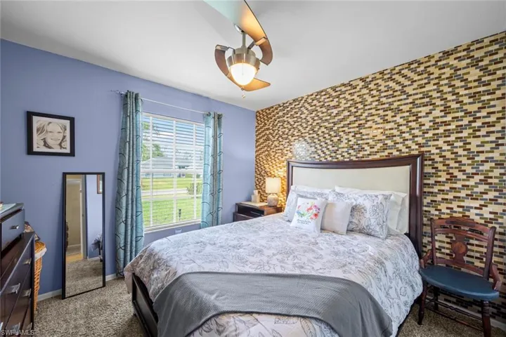 Carpeted bedroom featuring a ceiling fan, baseboards, and an accent wall