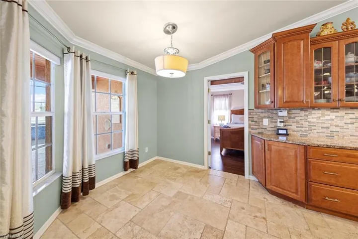 Kitchen with baseboards, a wealth of natural light, crown molding, stone tile floors, and backsplash