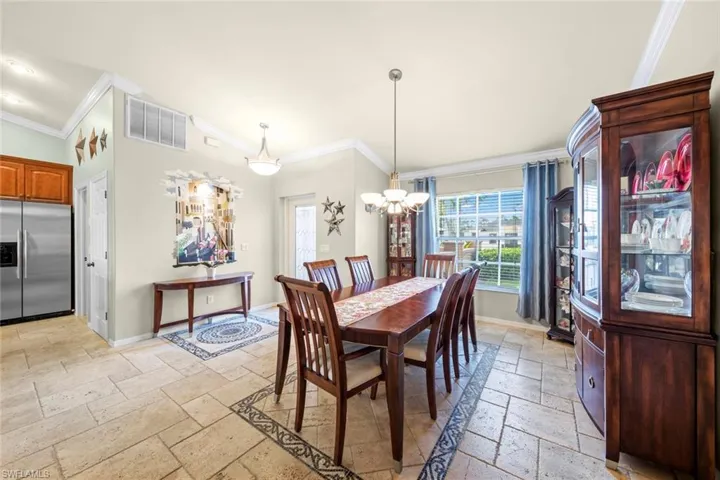 Dining space with baseboards, a notable chandelier, stone tile flooring, and crown molding