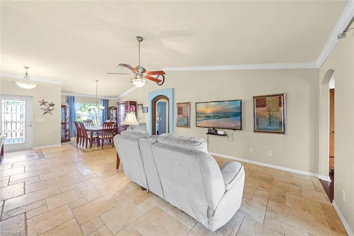Living area featuring arched walkways, stone tile floors, baseboards, and ornamental molding