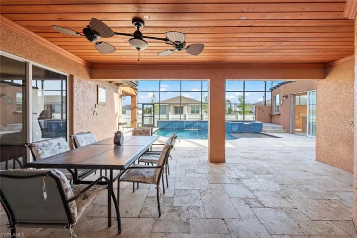View of patio with outdoor dining space, a pool with connected hot tub, glass enclosure, and ceiling fan