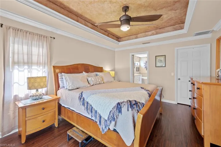 Bedroom featuring dark wood-style flooring, visible vents, a tray ceiling, and ornamental molding