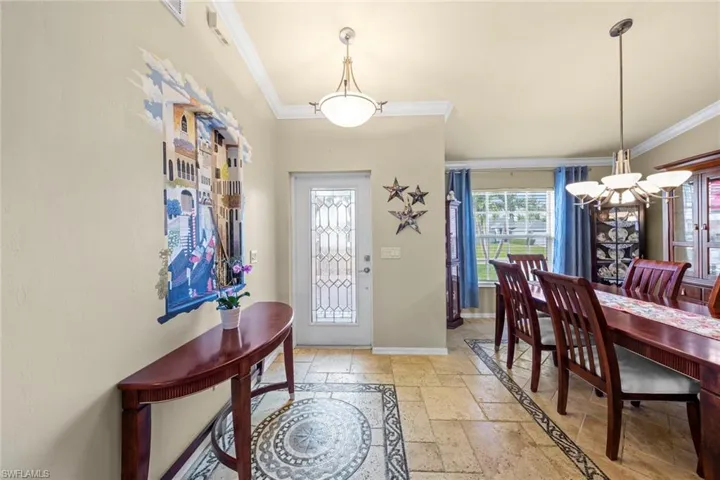Foyer with travertine tile flooring, a notable chandelier, baseboards, and ornamental molding
