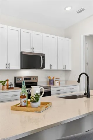 Kitchen featuring light stone countertops, white cabinets, stainless steel appliances, and recessed lighting