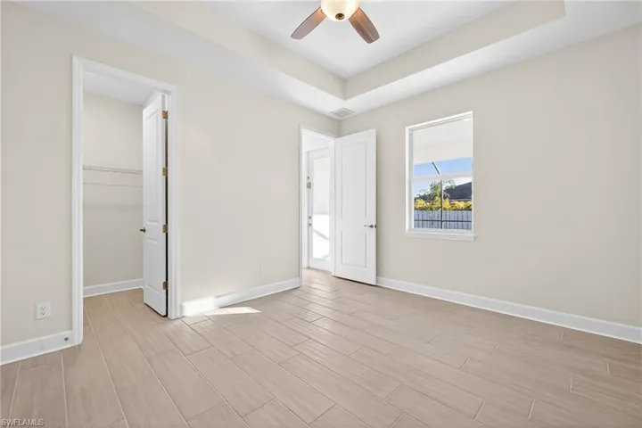 Unfurnished bedroom featuring a spacious closet, a raised ceiling, wood tiled floors, and a ceiling fan