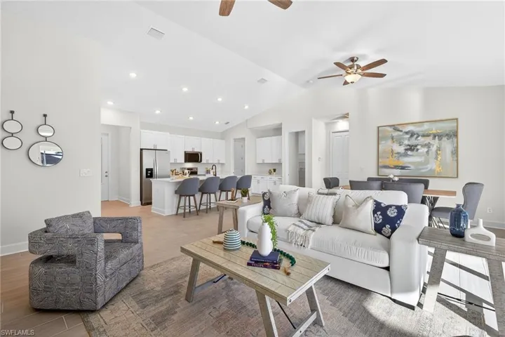 Living area with vaulted ceiling, a ceiling fan, light wood finished floors, and recessed lighting