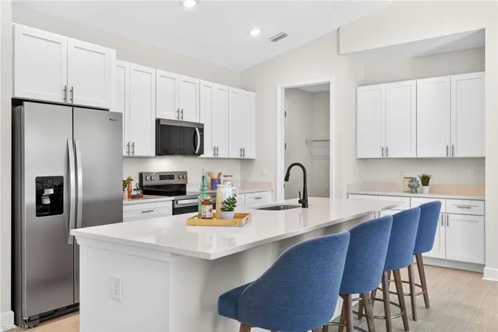 Kitchen with stainless steel appliances, light wood-style floors, white cabinetry, an island with sink, and recessed lighting