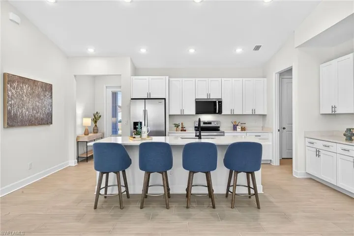 Kitchen featuring a breakfast bar, white cabinetry, light wood-style floors, a kitchen island with sink, and appliances with stainless steel finishes