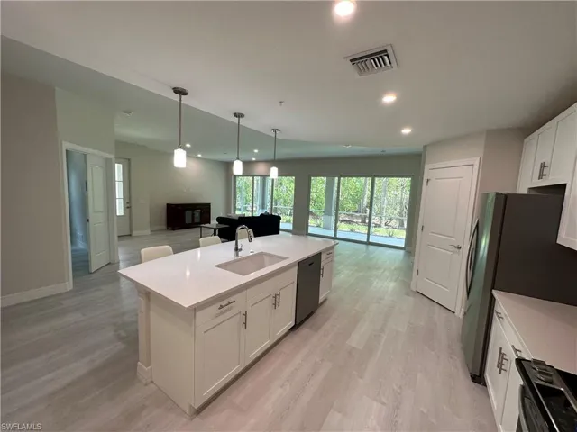 Kitchen with open floor plan, white cabinets, an island with sink, light wood-style flooring, and black appliances