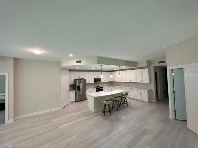 Kitchen featuring white cabinetry, a kitchen breakfast bar, stainless steel appliances, an island with sink, and light wood-type flooring