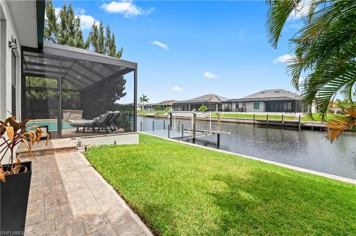 View of grassy yard with a dock, glass enclosure, a water view, a sunroom, and boat lift