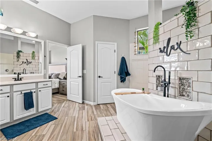Ensuite bathroom with vanity, a freestanding bath, wood finish floors, and tile walls