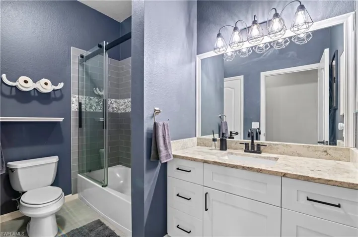 Bathroom featuring bath / shower combo with glass door, vanity, and a textured wall
