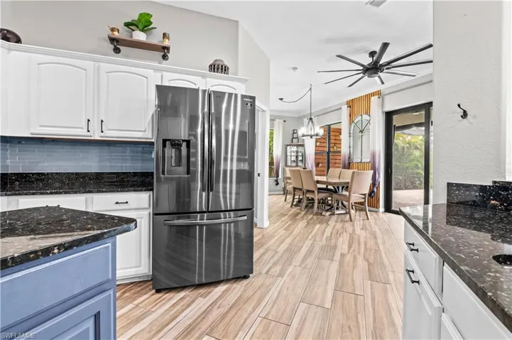Kitchen featuring dark stone counters, stainless steel refrigerator with ice dispenser, white cabinetry, hanging light fixtures, and ceiling fan