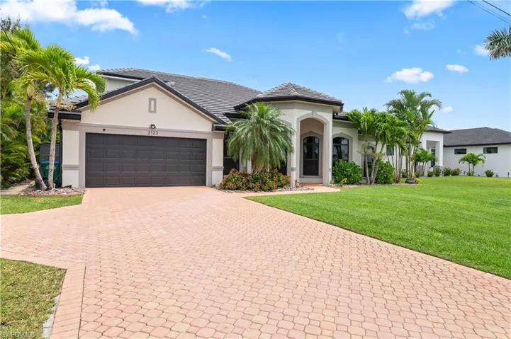 Mediterranean / spanish-style house with a front yard, stucco siding, decorative driveway, and an attached garage