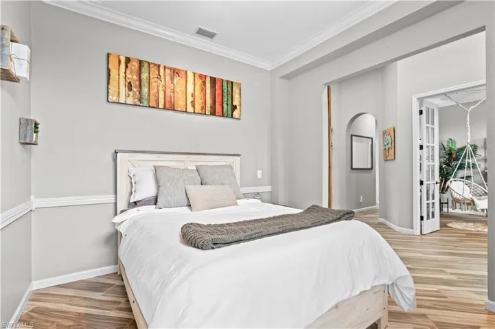 Bedroom featuring crown molding, light wood finished floors, and arched walkways