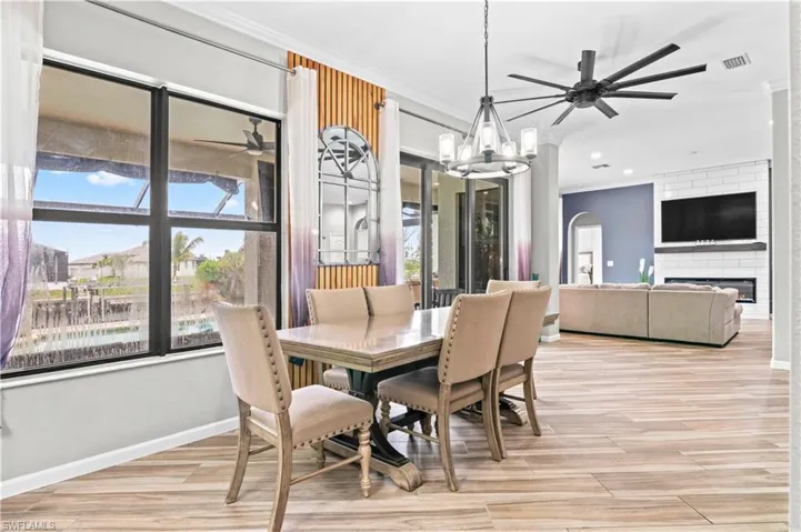 Dining room featuring ceiling fan, light wood finished floors, a chandelier, a large fireplace, and ornamental molding