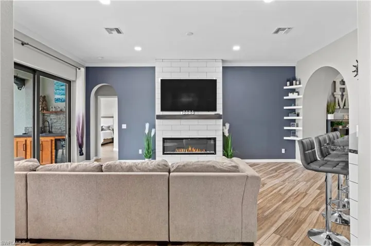 Living area with arched walkways, a large fireplace, wood finished floors, recessed lighting, and ornamental molding