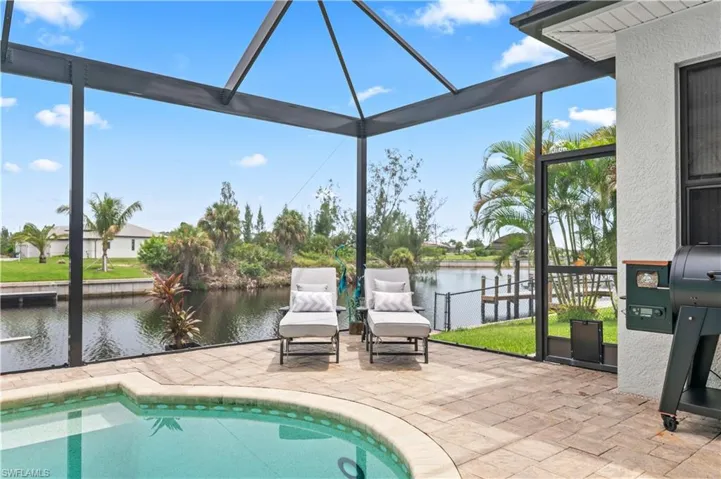 Outdoor pool with a patio area, a sunroom, a grill, a water view, and glass enclosure